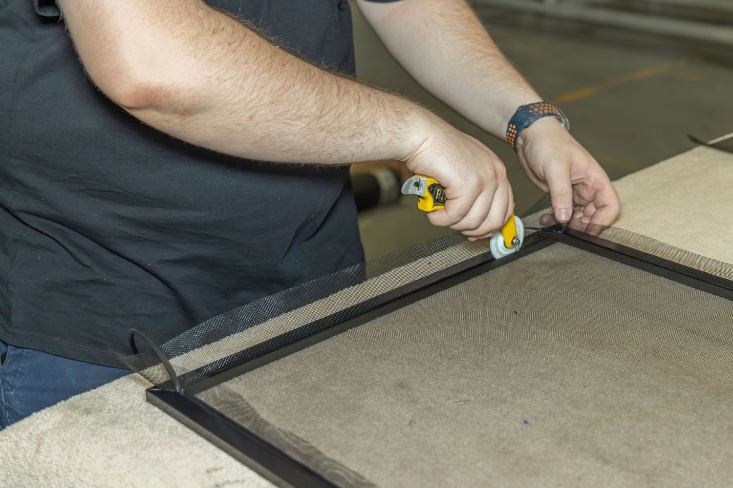 Man assembling a metal frame with a screwdriver on a workbench in a workshop setting.