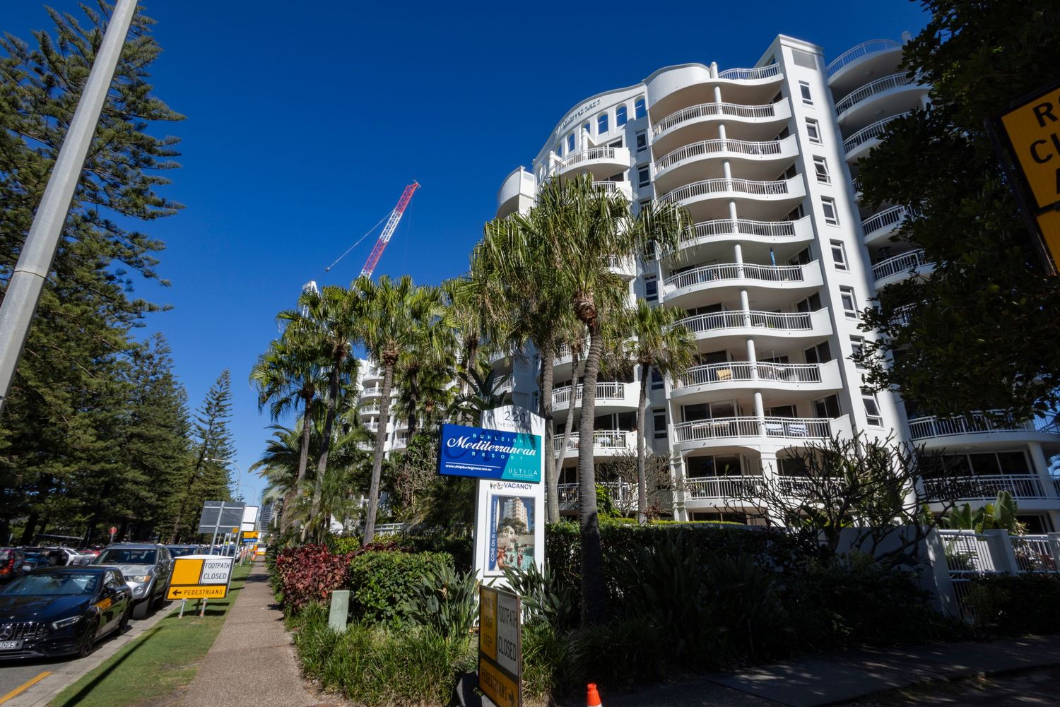 Tall white beachside apartment building surrounded by palm trees under a clear blue sky on the Gold Coast, Australia.