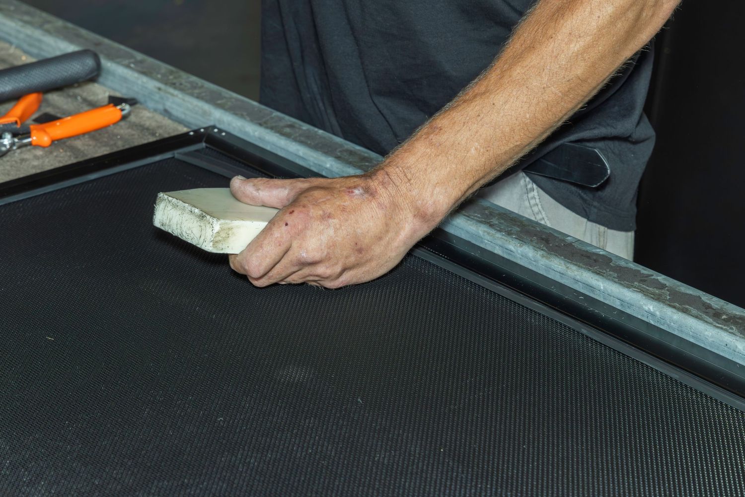 Worker sanding carbon fiber surface with white sanding block during professional composite material finishing process.