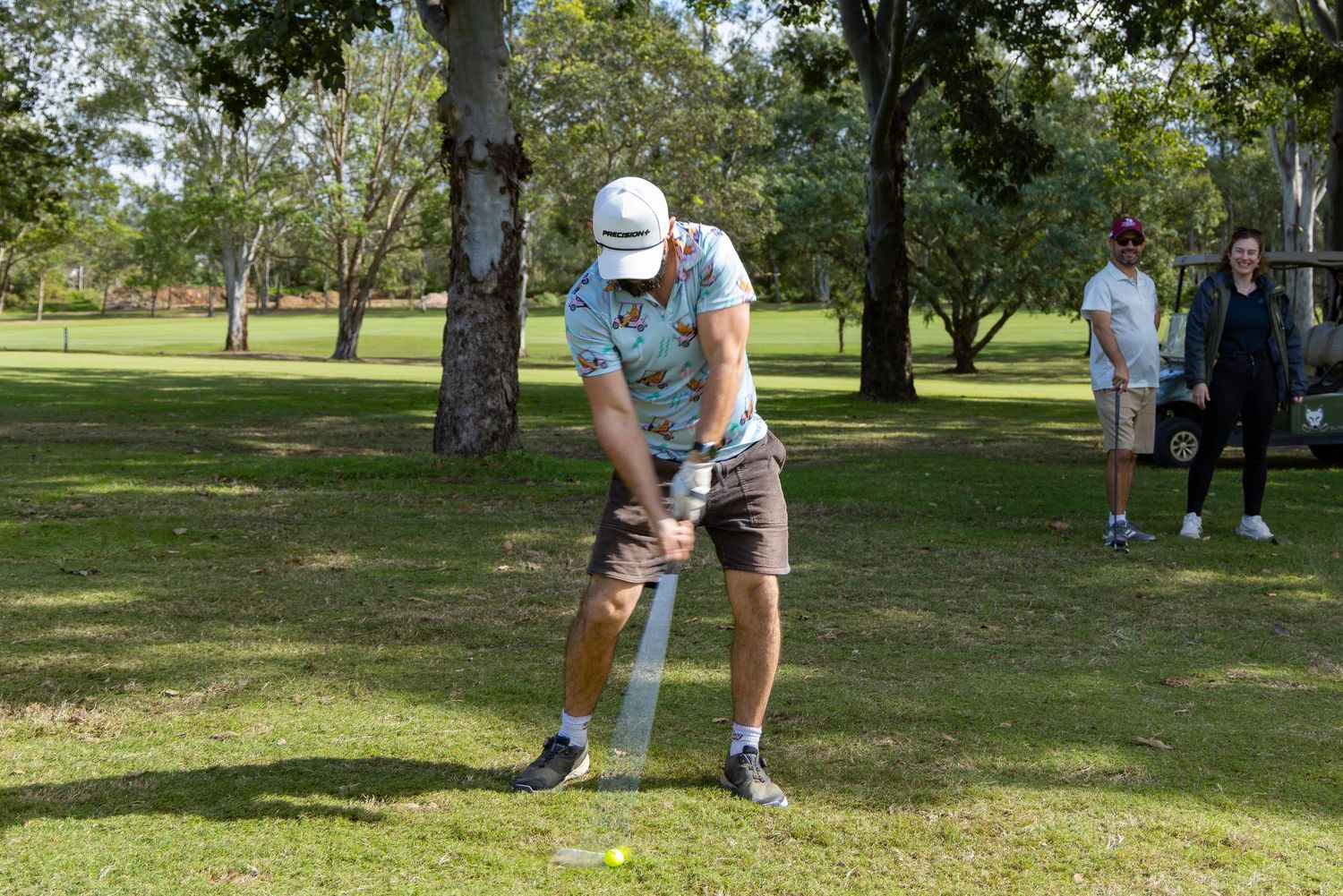Golfer addressing a golf ball on a lush green course with spectators watching in the background.