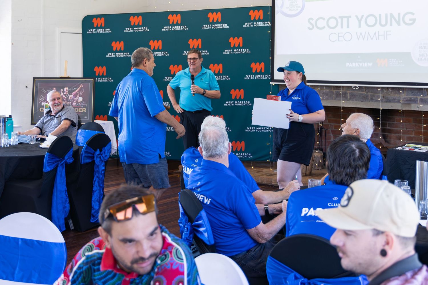Scott Young wine event with guests in blue shirts gathered around a presentation table indoors.