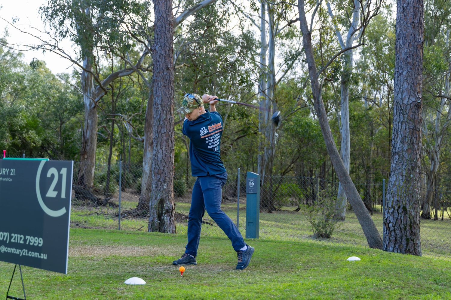 Golfer completing a powerful tee shot at hole 21 surrounded by Australian eucalyptus trees.