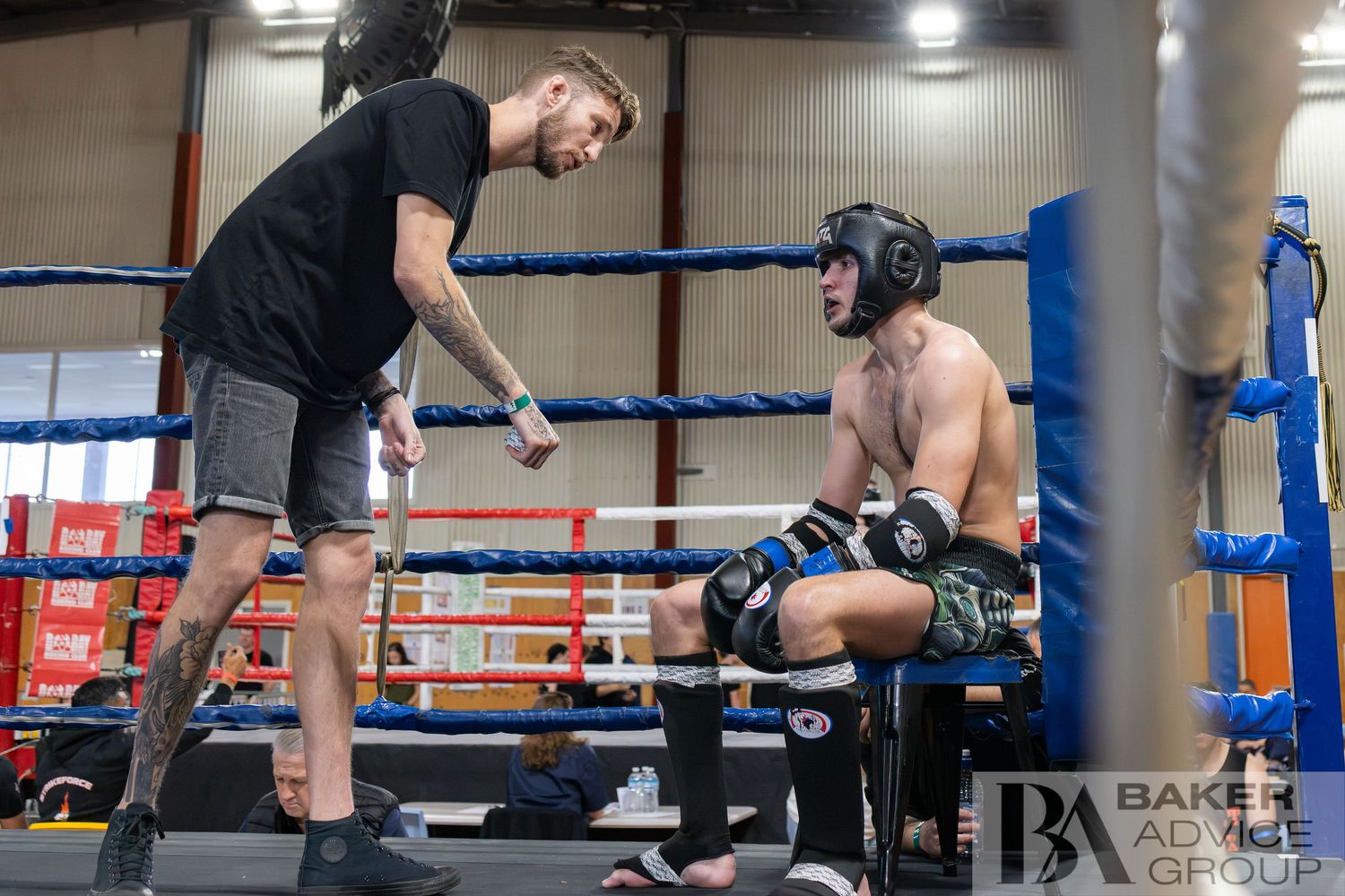 A boxing coach gives corner advice to a fighter in headgear during a sparring session in a gym ring.