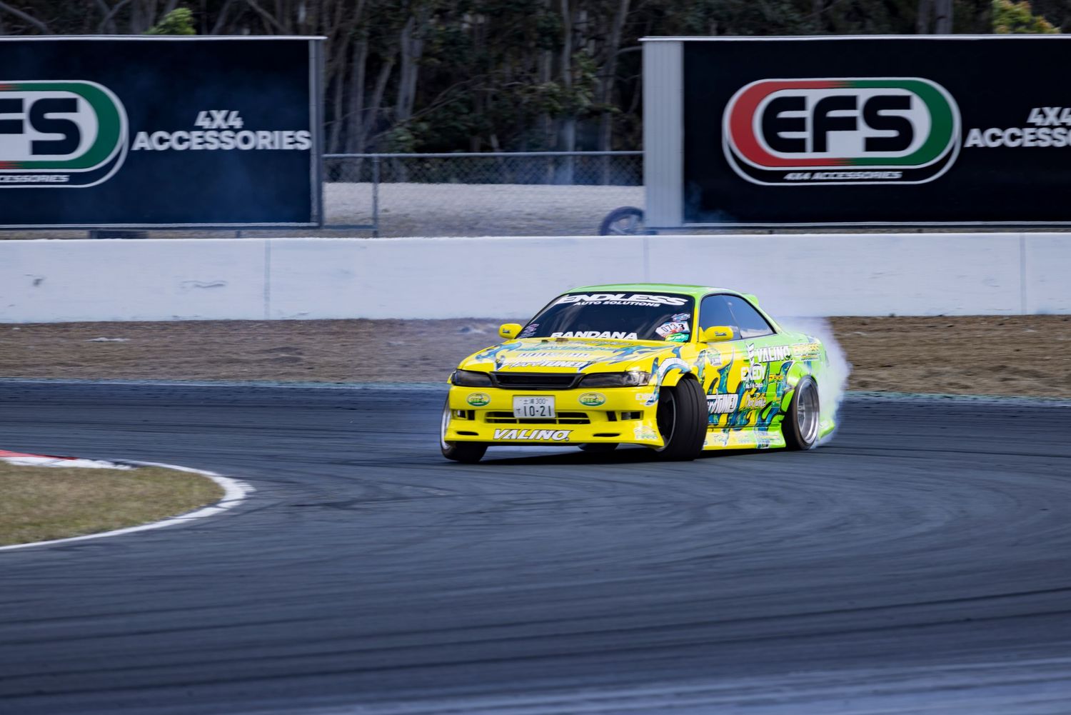 Yellow drift car racing on a track with EFS 4x4 Accessories signage, producing tire smoke during a competition.