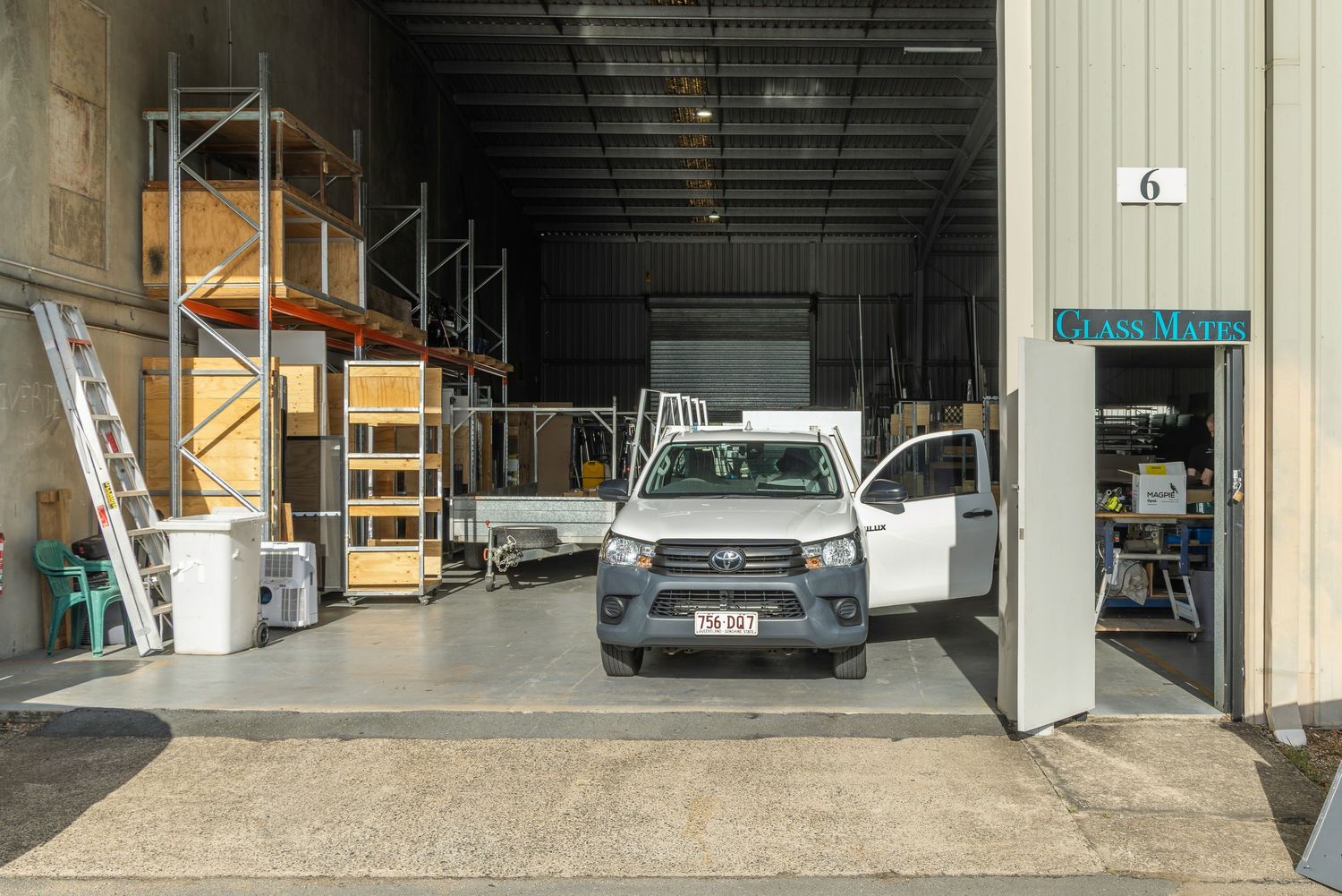 White pickup truck parked inside an industrial warehouse unit number 6 with storage shelving and equipment visible.