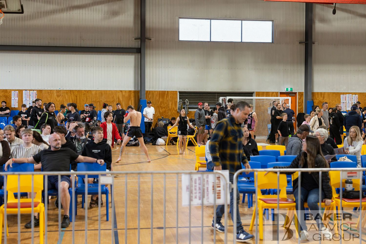 Crowd of people seated on colorful chairs inside a large sports hall during an indoor event.