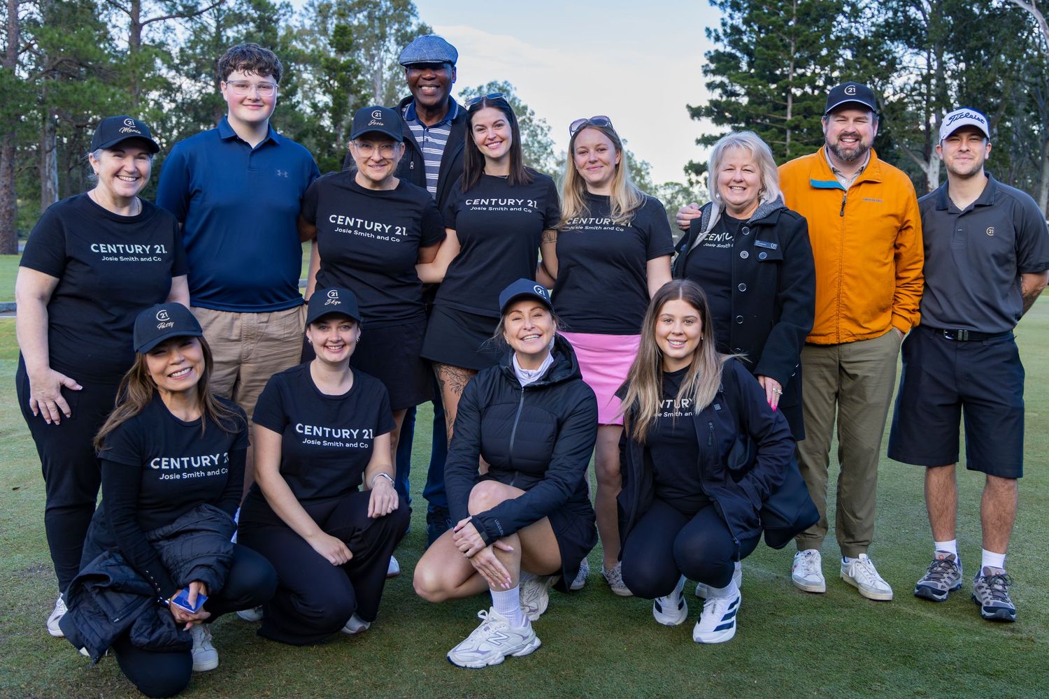 Group photo of Century 21 real estate team members in branded black shirts posing together on a golf course at dusk.
