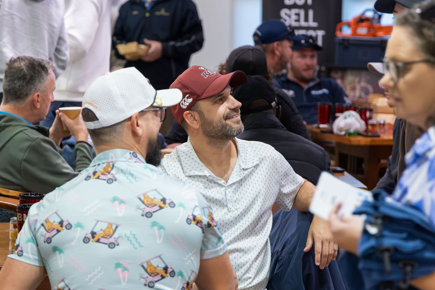 Two men in caps chat and smile at a casual indoor social gathering event.