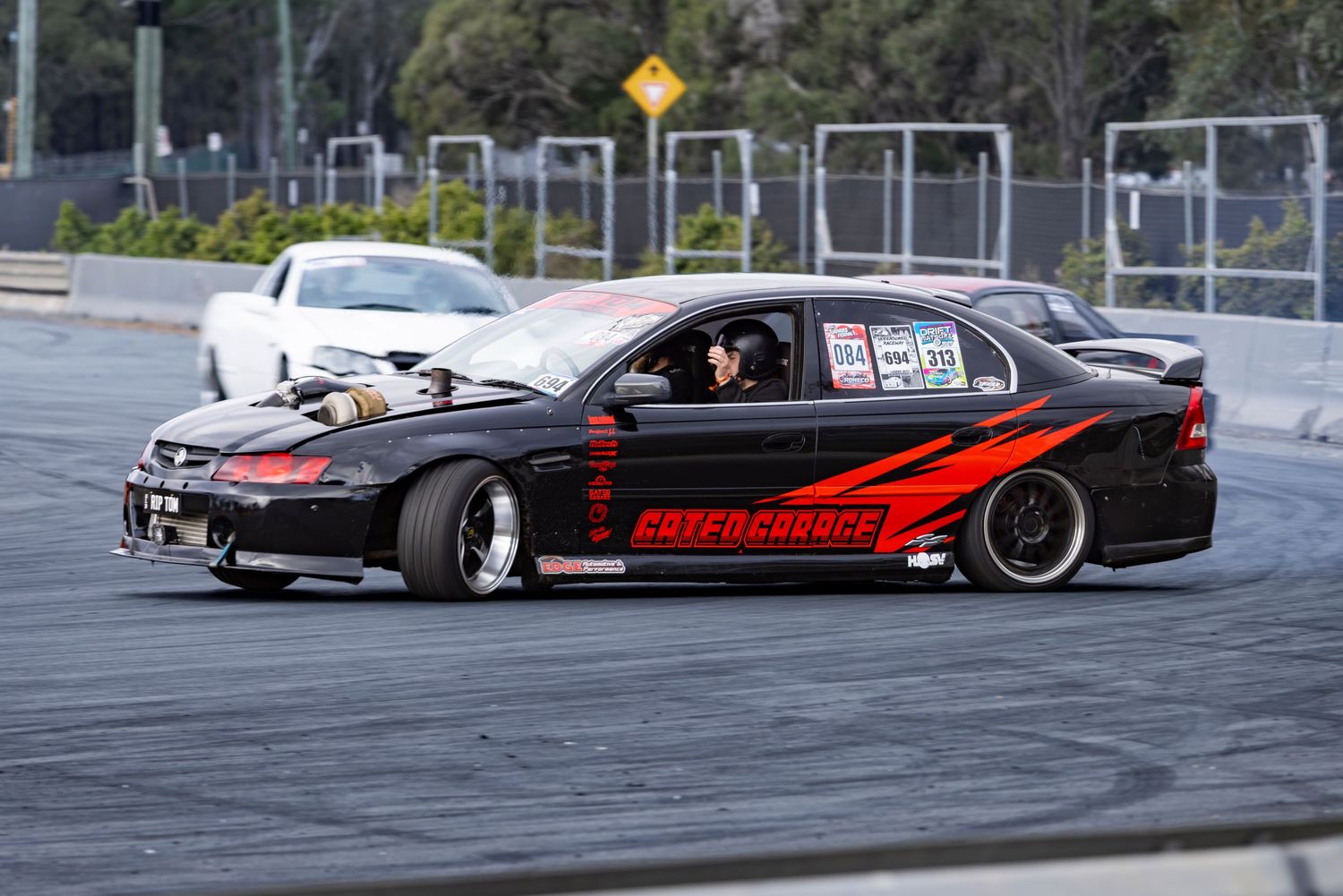 Black drift car with red flames livery competing on a race track during a motorsport event.