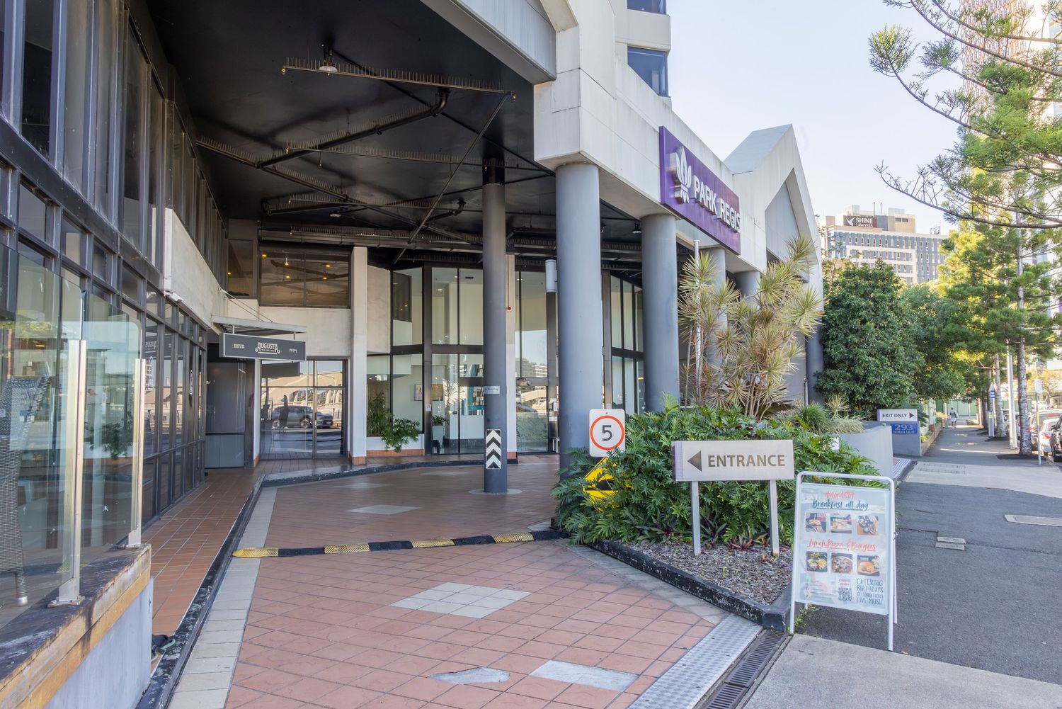 Modern commercial building entrance with brick walkway, glass doors, and entrance signage in an urban setting.