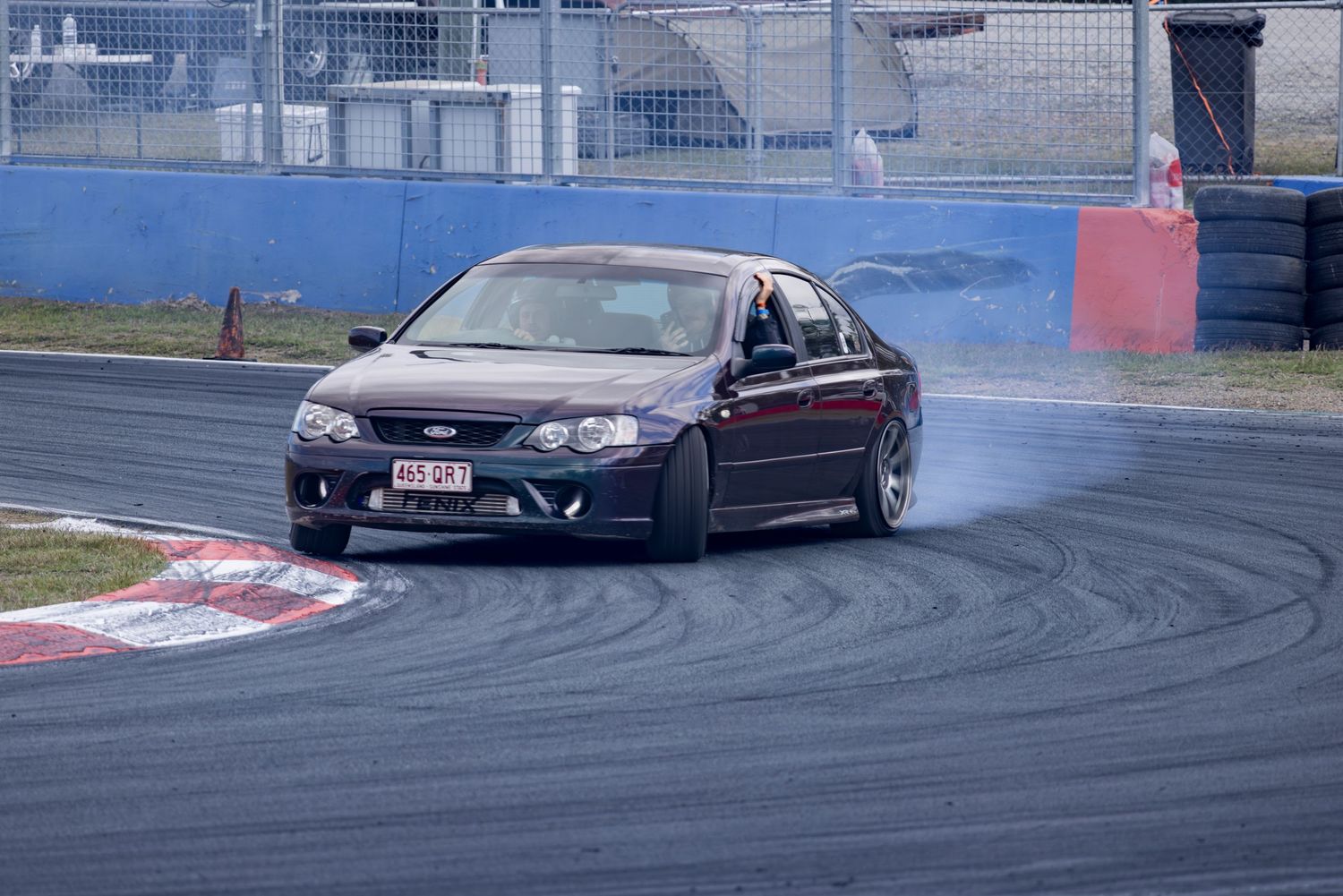 Dark sedan drifts around a corner leaving tire smoke on a racing circuit.