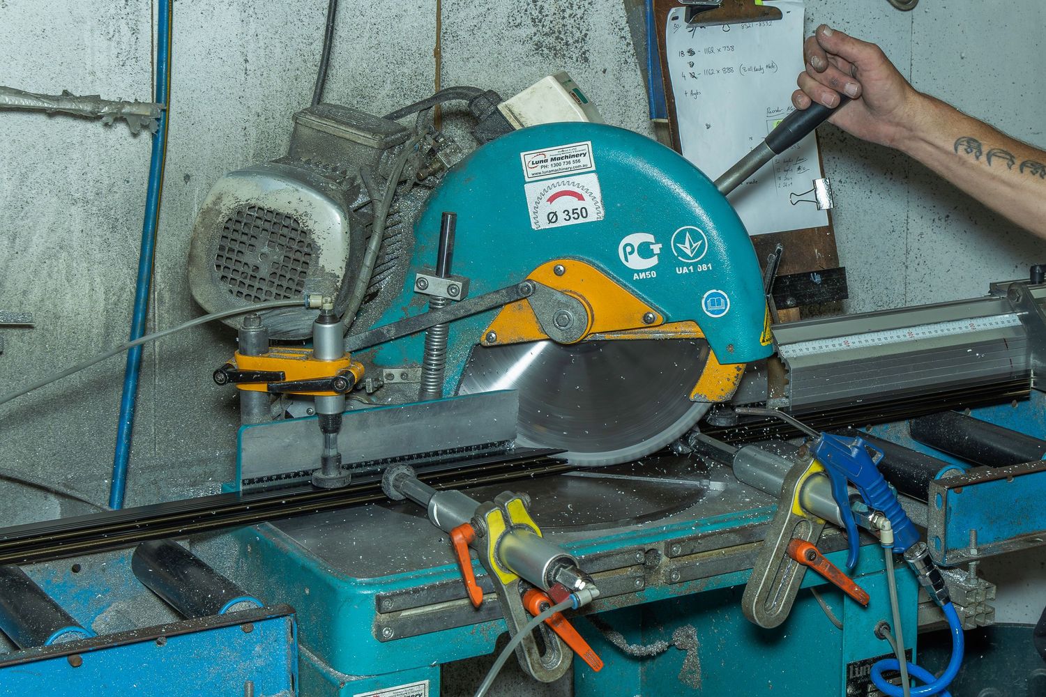 A person operating a blue industrial miter saw cutting machine in a workshop.