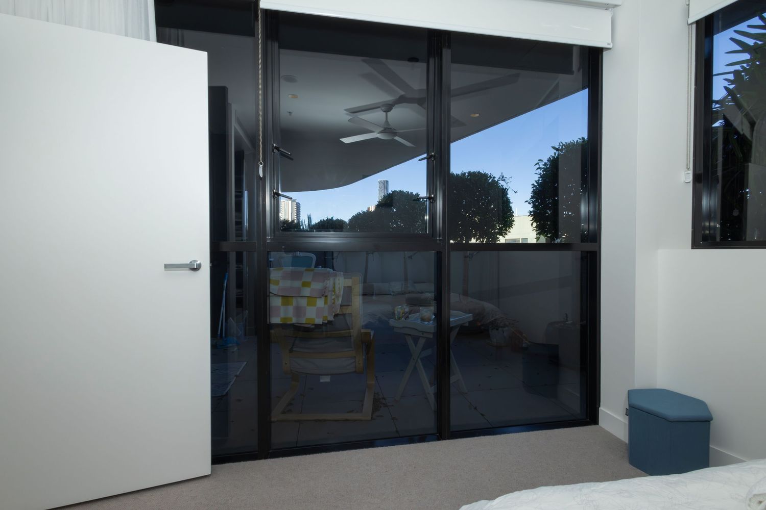 Black aluminum sliding glass doors opening to an outdoor patio area with ceiling fan and blue furniture.