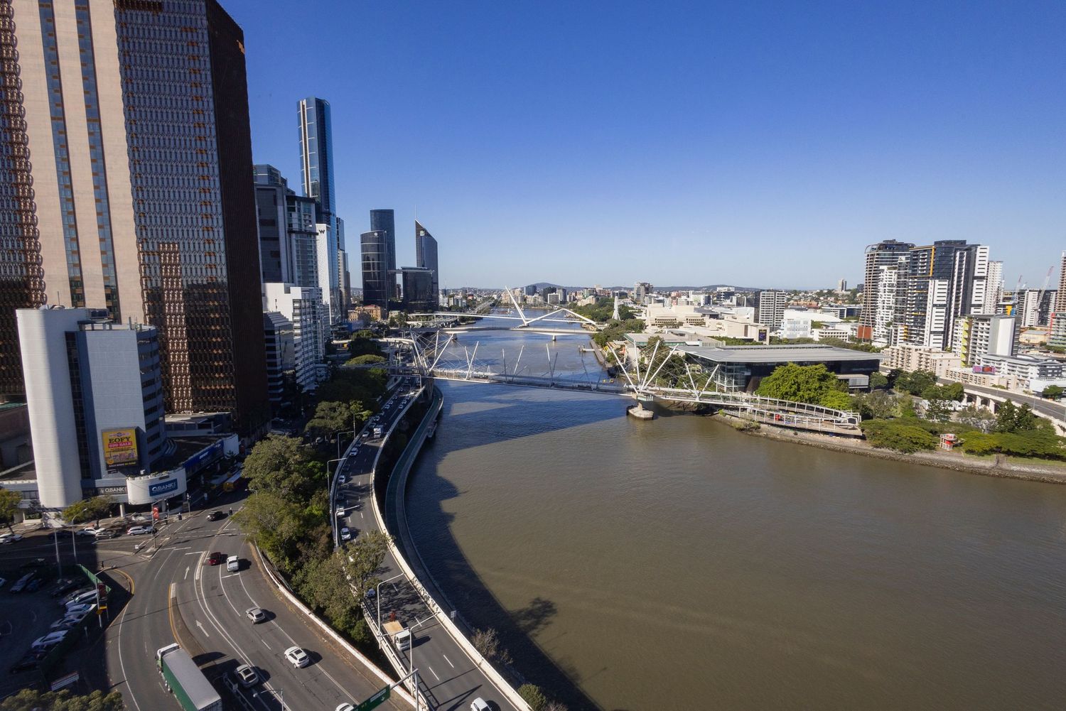 Aerial view of Brisbane River winding through the city CBD with bridges, skyscrapers, and clear blue sky.