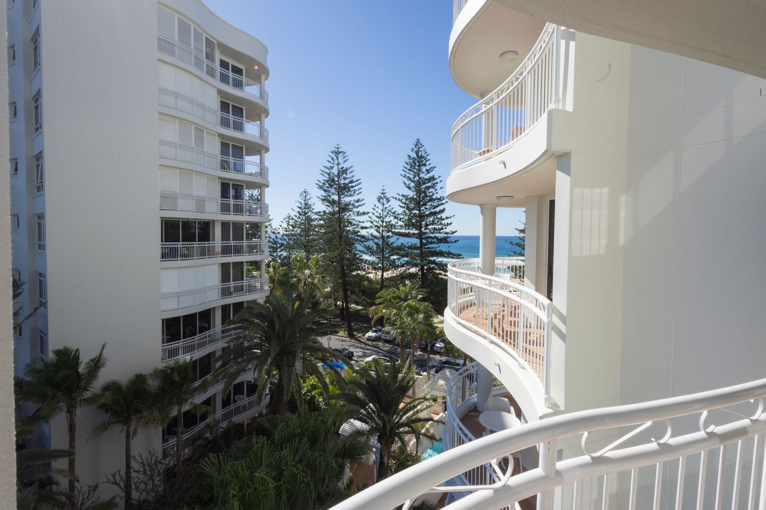 Balcony view of resort pool, palm trees, and ocean from a white high-rise building on the Gold Coast.