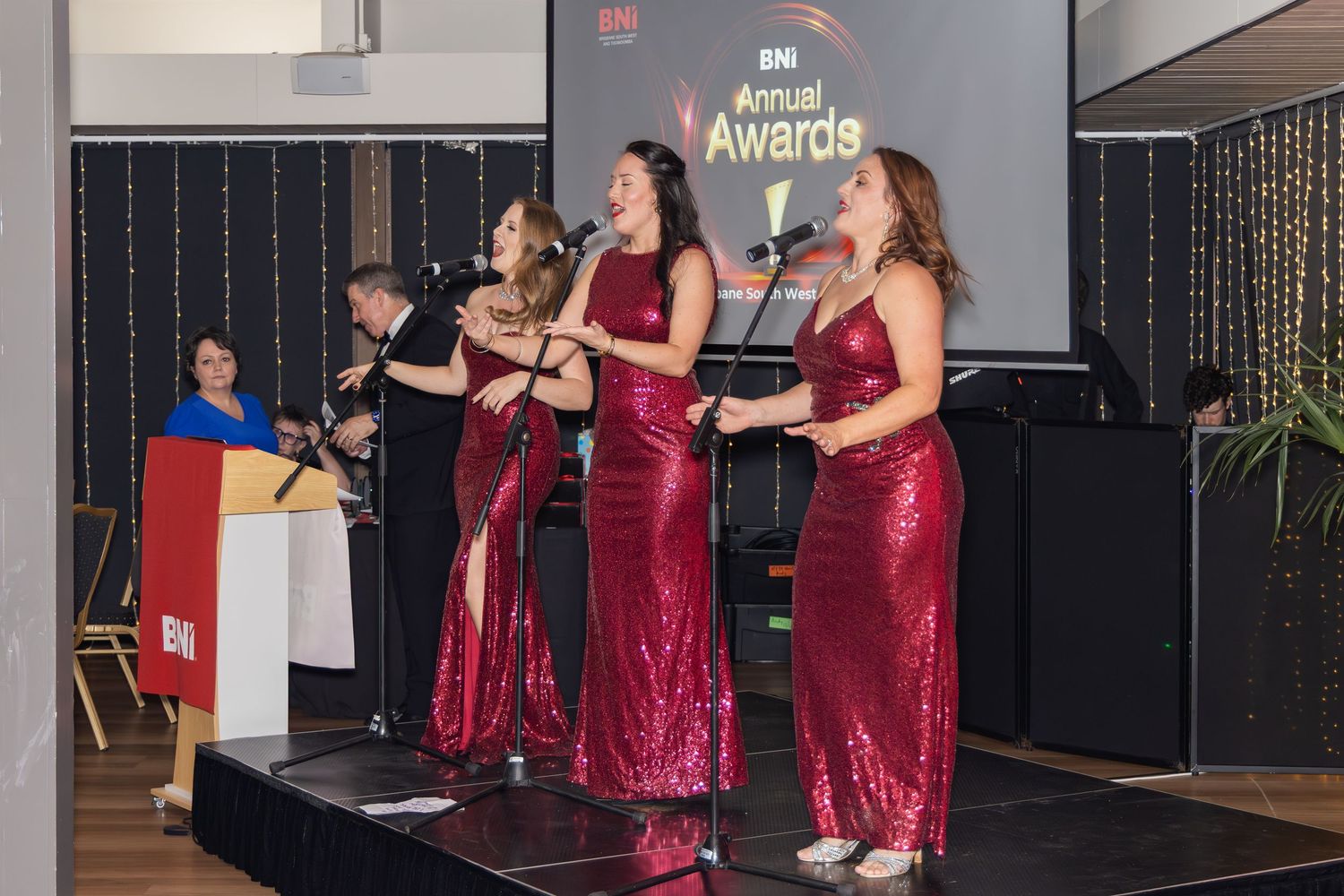 Four women in red sequin gowns performing on stage at IEMI Annual Awards ceremony.