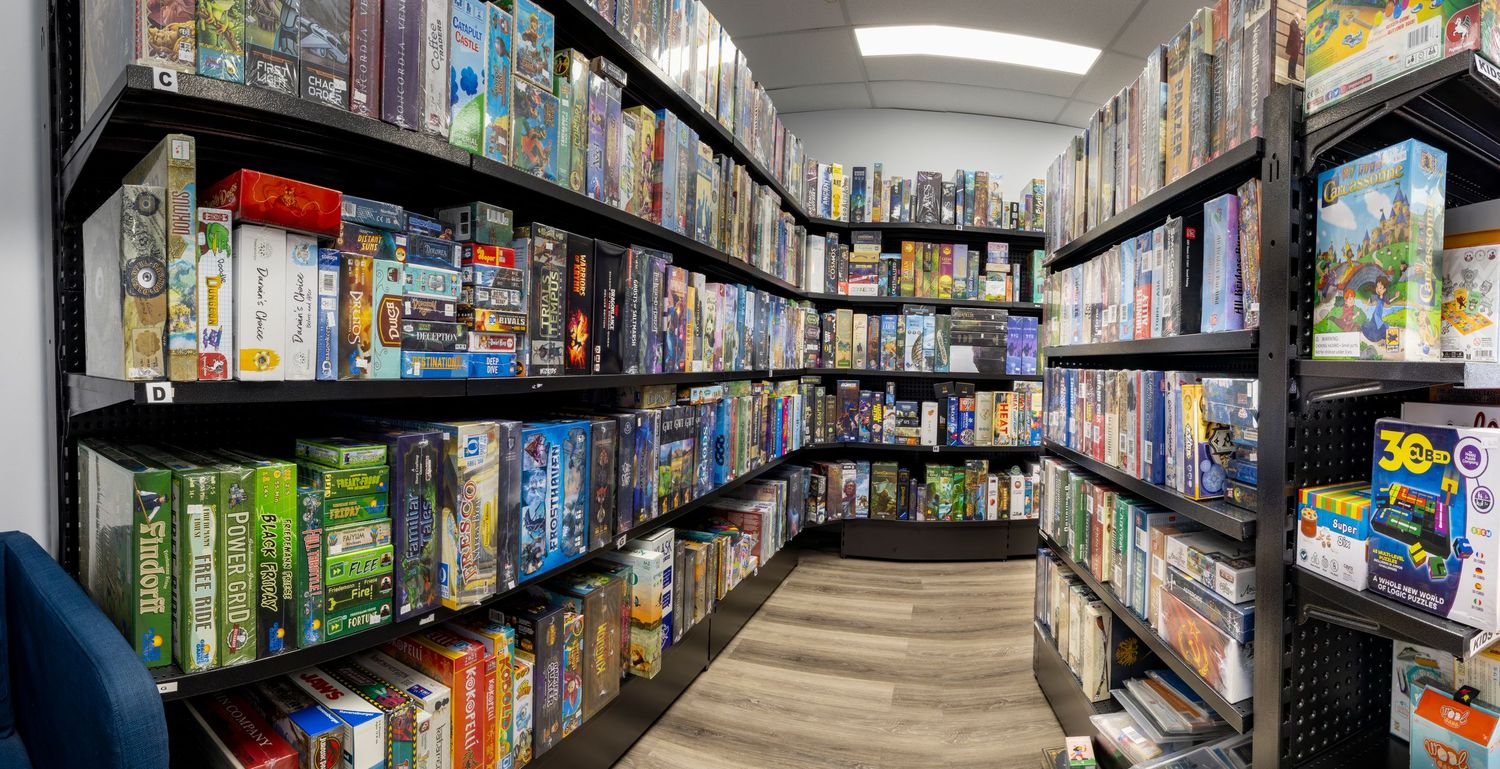 Rows of colorful board games filling tall black shelves in a well-organized game store aisle.