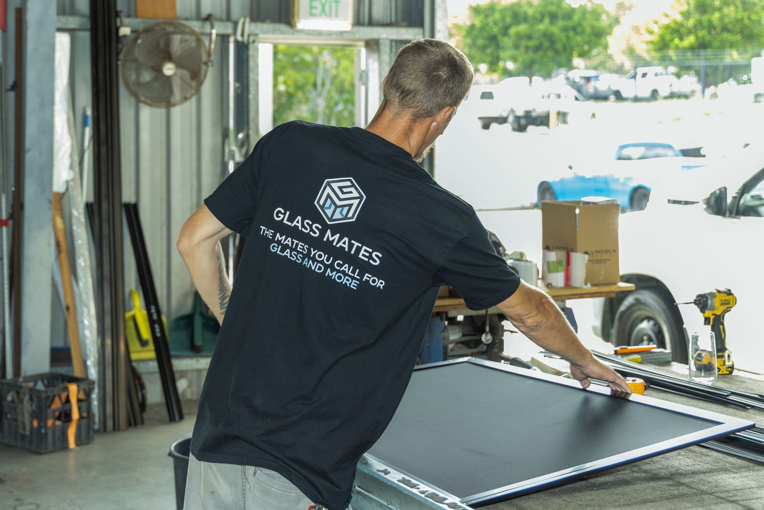 Glass Mates technician handling a large glass panel in a workshop, wearing branded black t-shirt.
