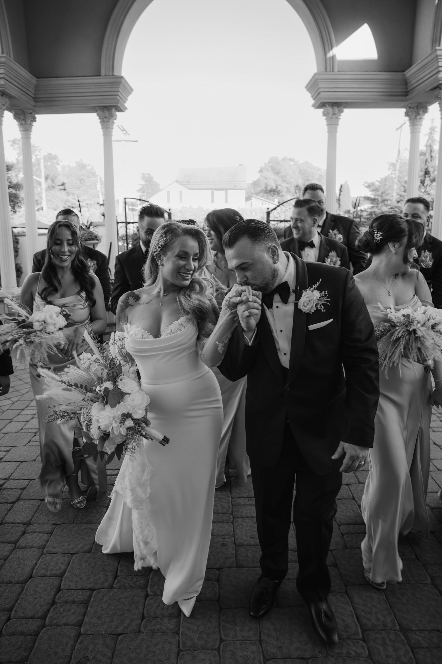 Black and white photo of a bride and groom walking down the aisle after their wedding ceremony with bridal party.