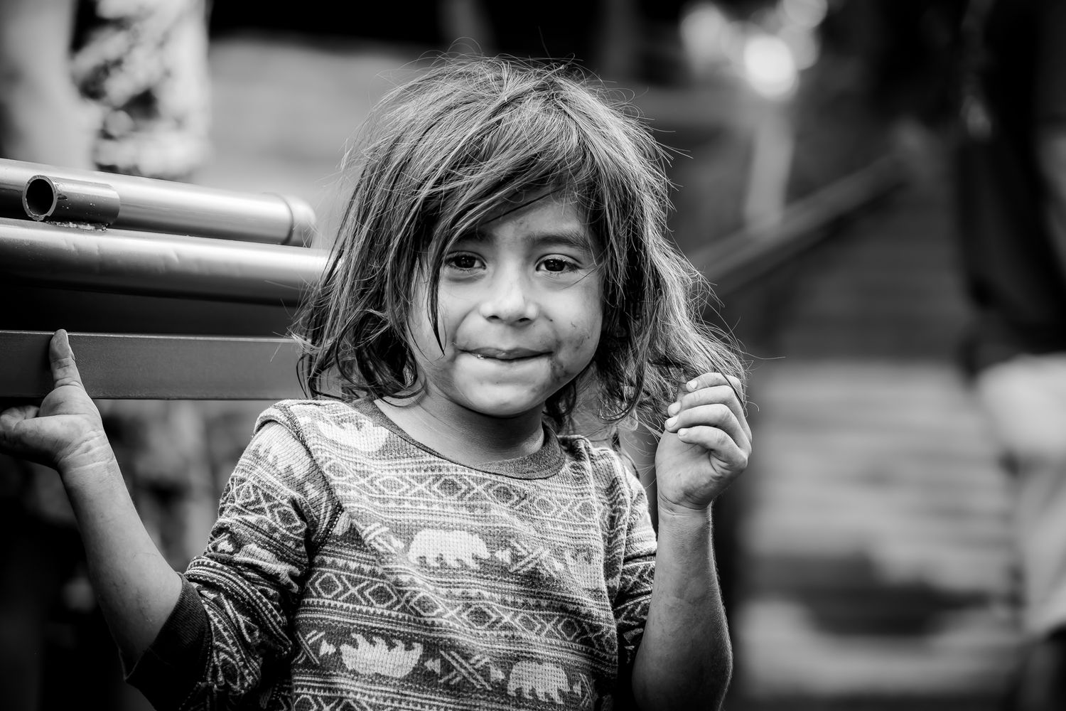 Smiling young girl with tousled hair wearing a patterned shirt in black and white.