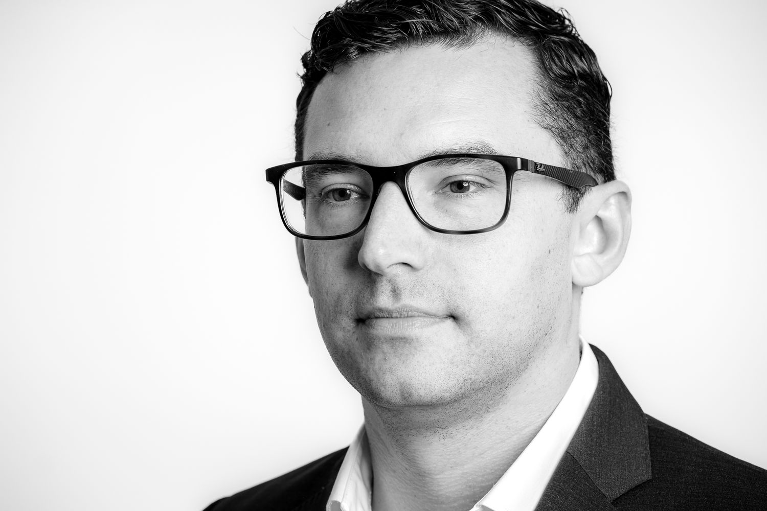 Black and white professional headshot of a man wearing glasses and a suit jacket.