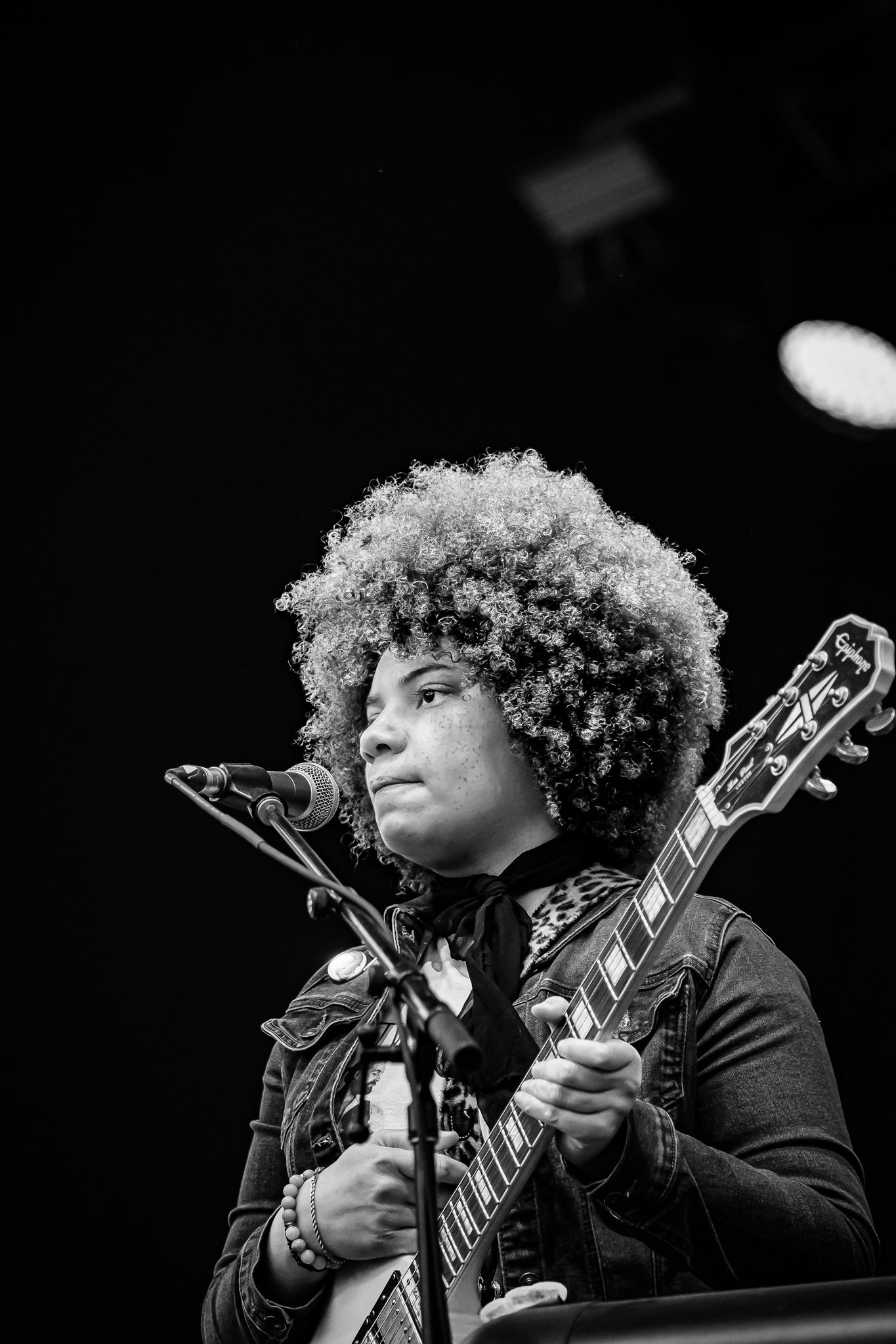 Young musician with afro hairstyle playing electric guitar on stage at live music event.