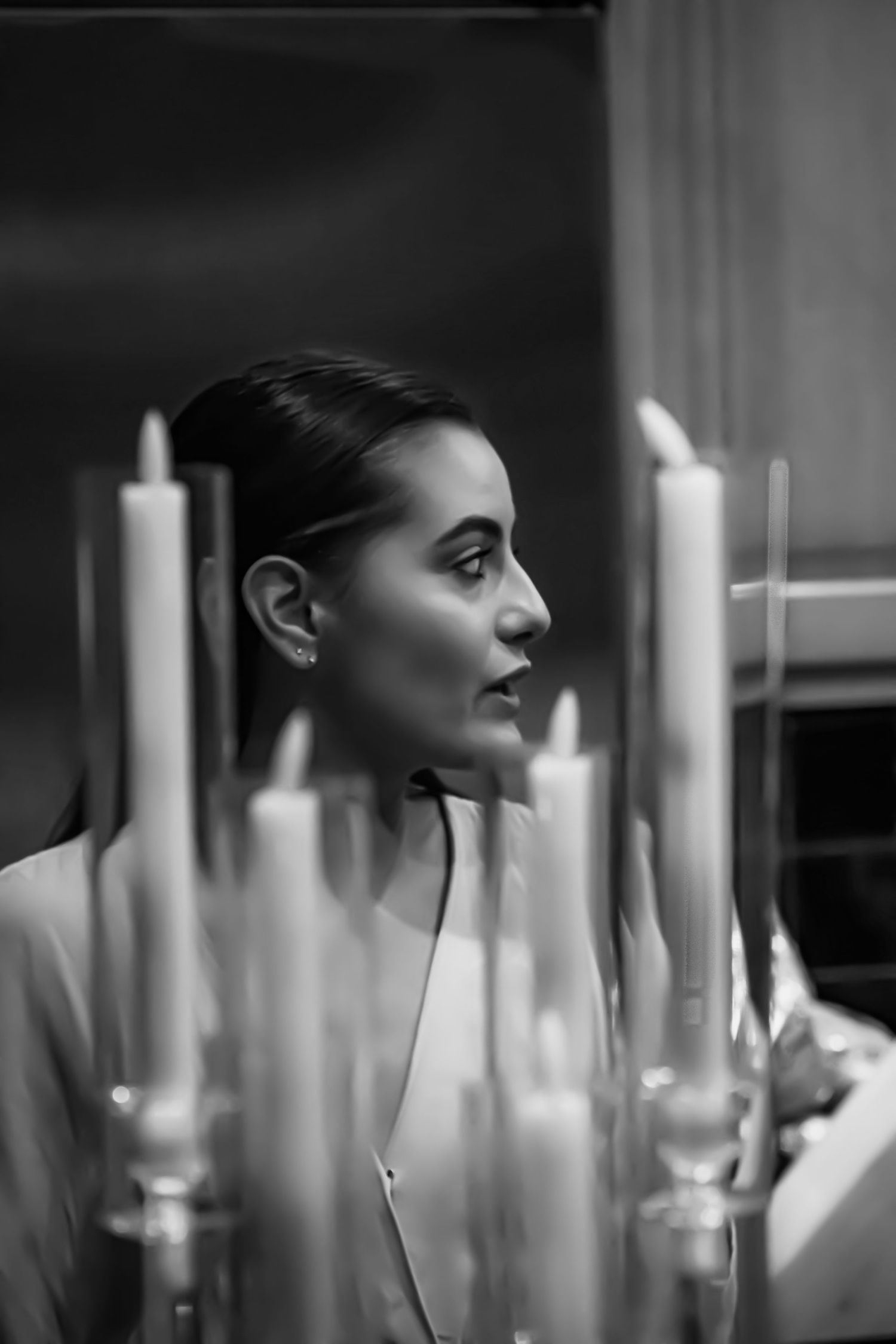 Elegant woman in profile view surrounded by tall candles in a moody black and white portrait.