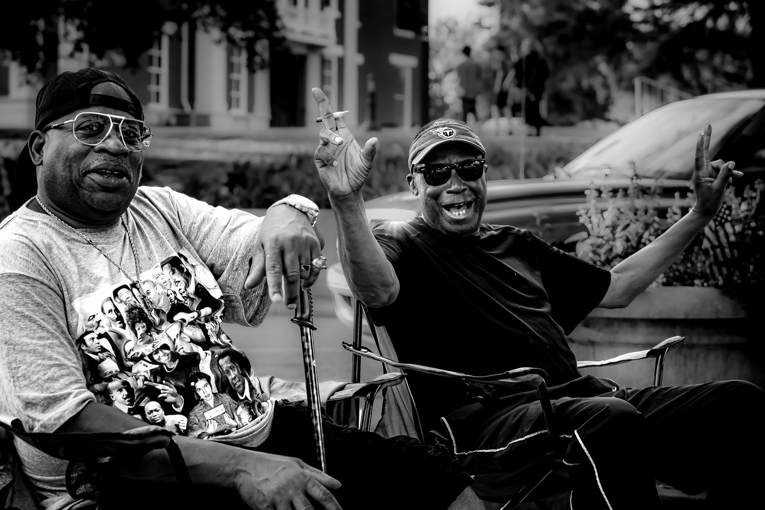 Two men smiling and posing outdoors in black and white photo, wearing sunglasses and casual attire.