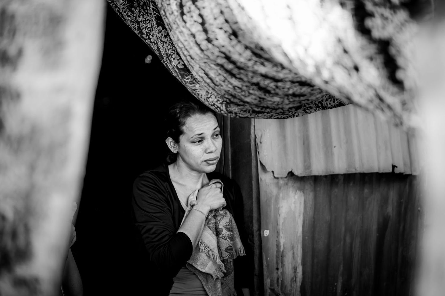 Black and white portrait of a woman standing in a doorway, looking pensive in dramatic shadows.