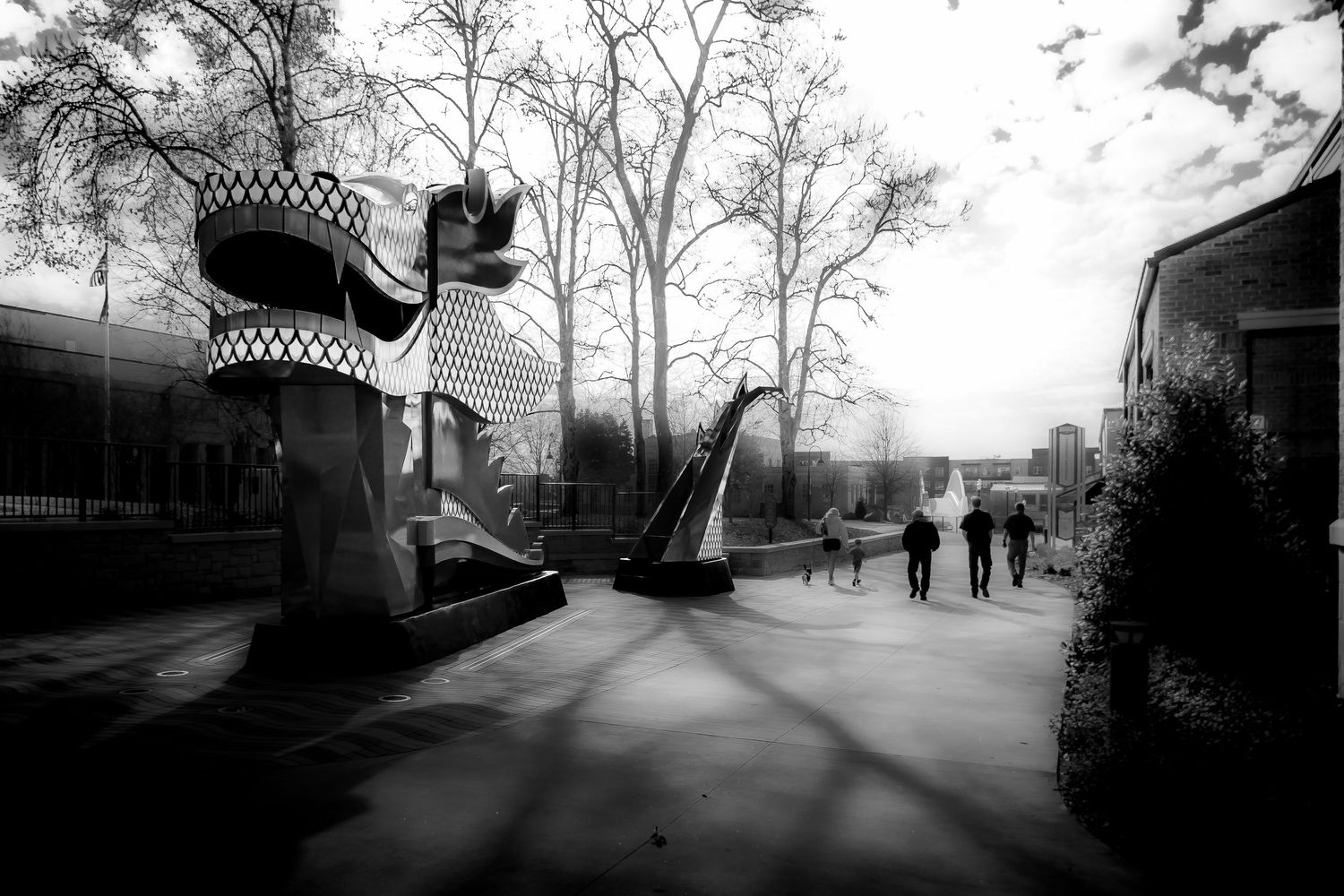 Black and white photo of abstract sculptures in an outdoor plaza with bare trees and buildings in the background.