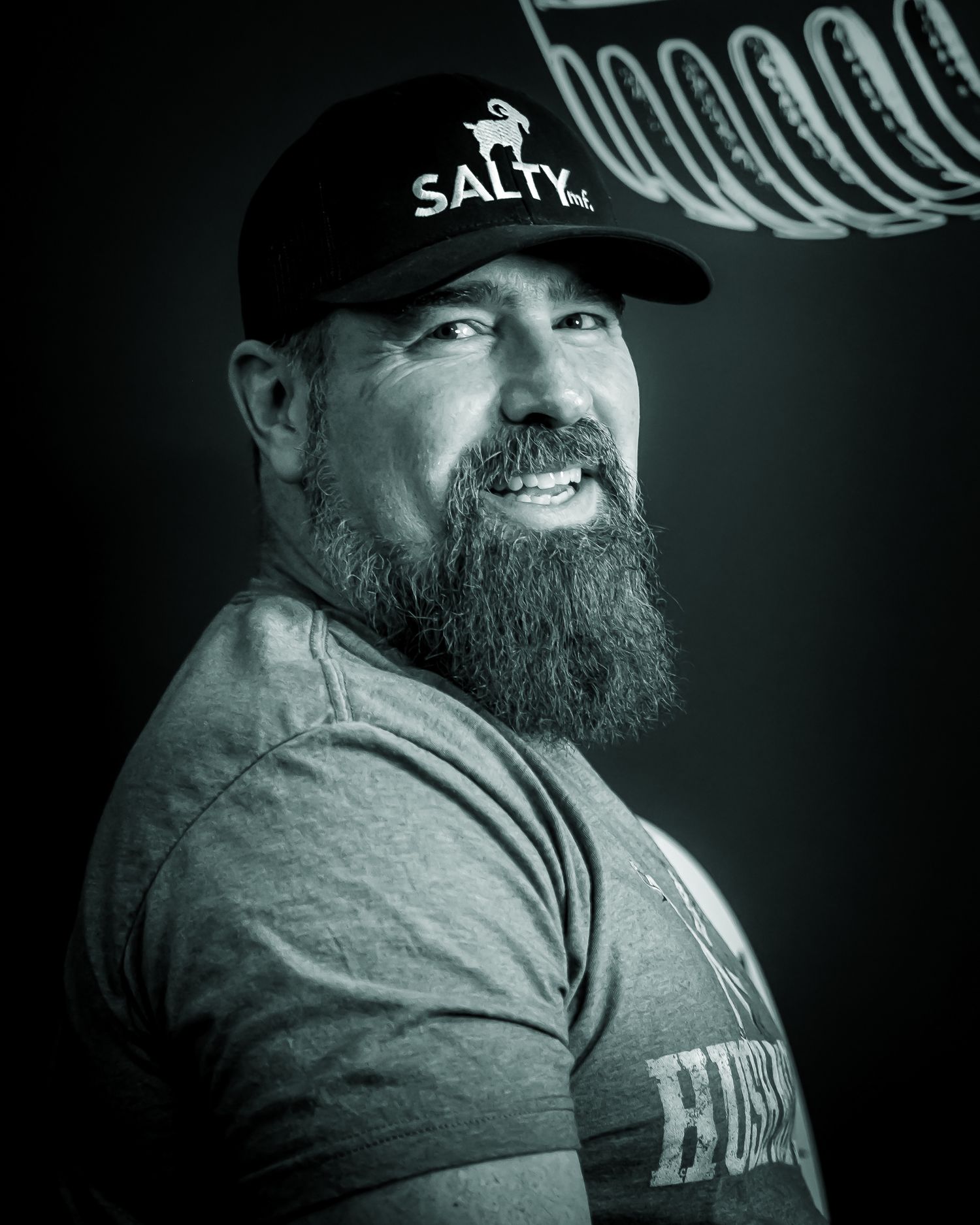 Bearded man in Salty baseball cap smiles confidently in dramatic black and white portrait photo. Podcast coverage