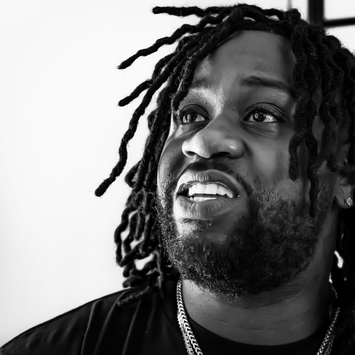 Black and white close-up portrait of a man with dreadlocks and beard looking upward.
