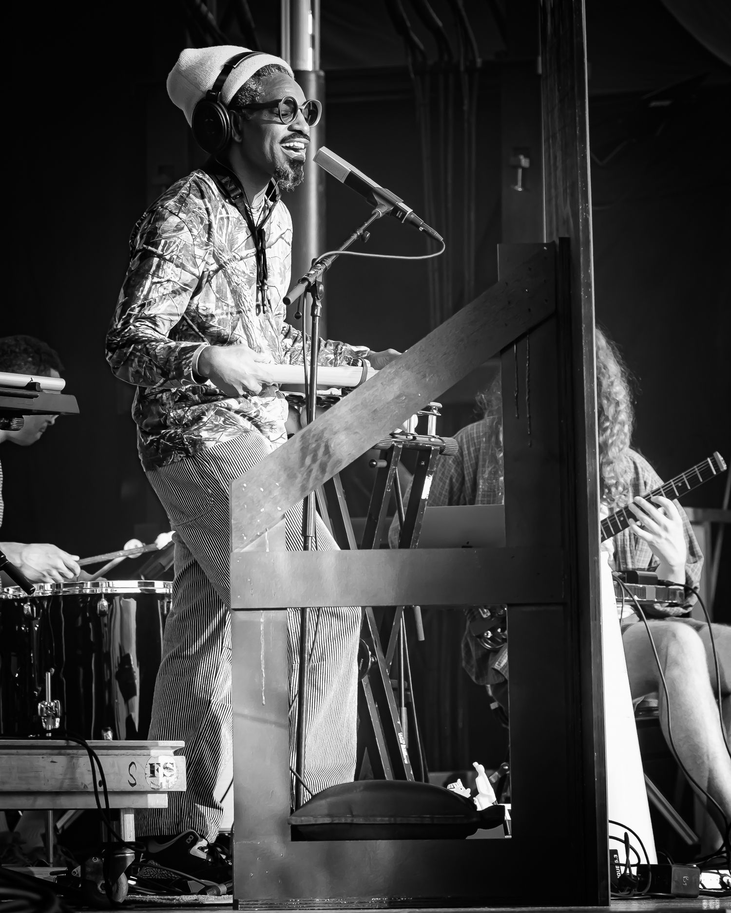 Black and white concert photo of a musician singing at a microphone while playing keyboard on stage.