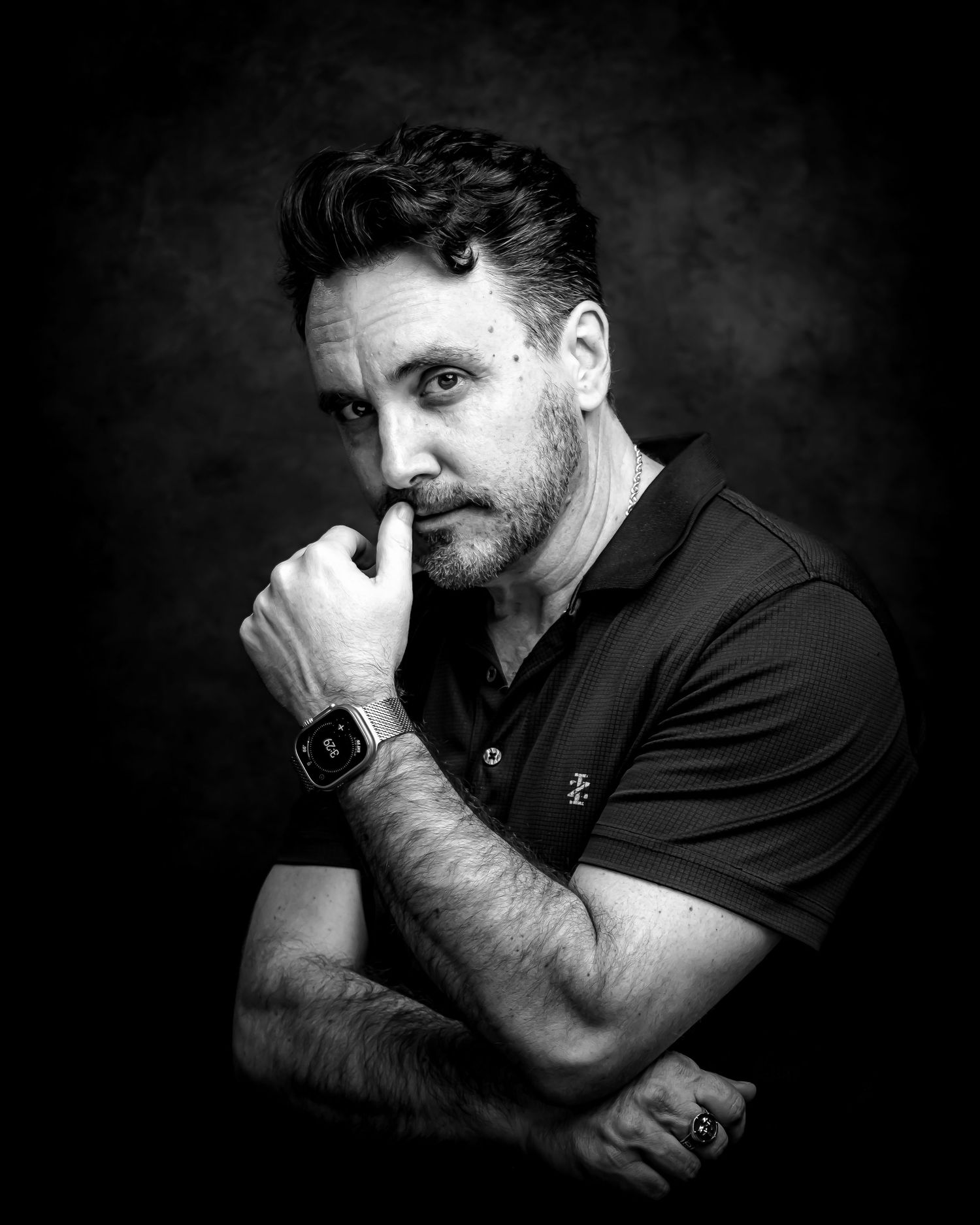 Black and white portrait of a thoughtful man in a polo shirt, hand on chin, wearing a smartwatch.