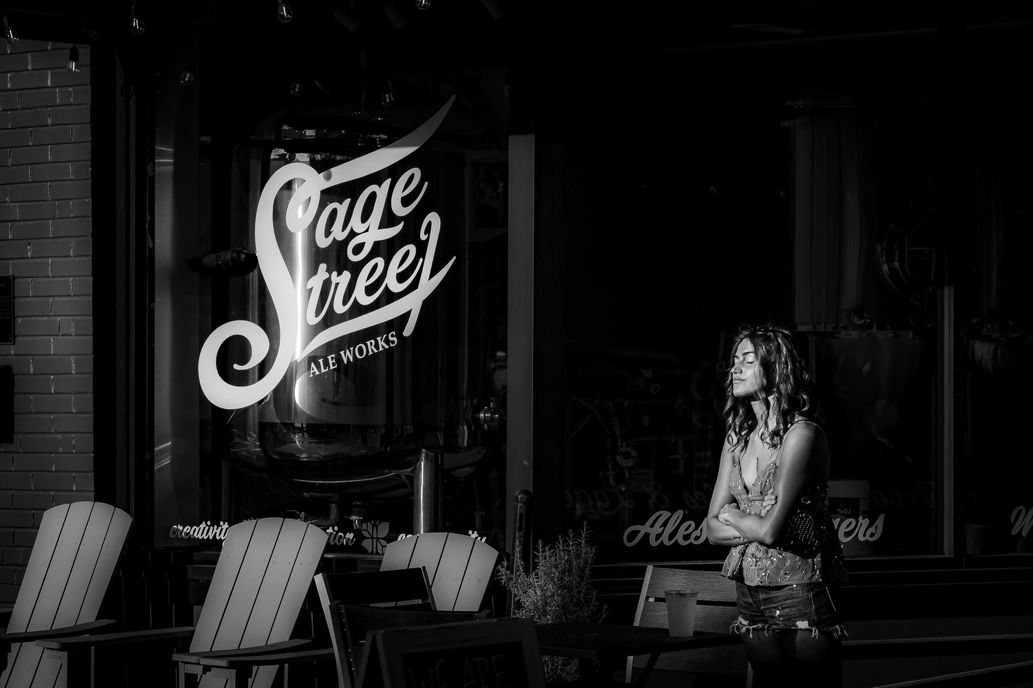 Black and white photo of a woman sitting outside Stage Street Ale Works brewery on a quiet street.