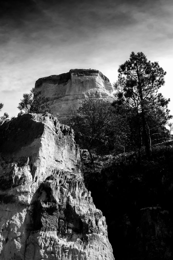 Black and white landscape of a flat-topped rock cliff with trees and eroded stone face against dramatic sky.
