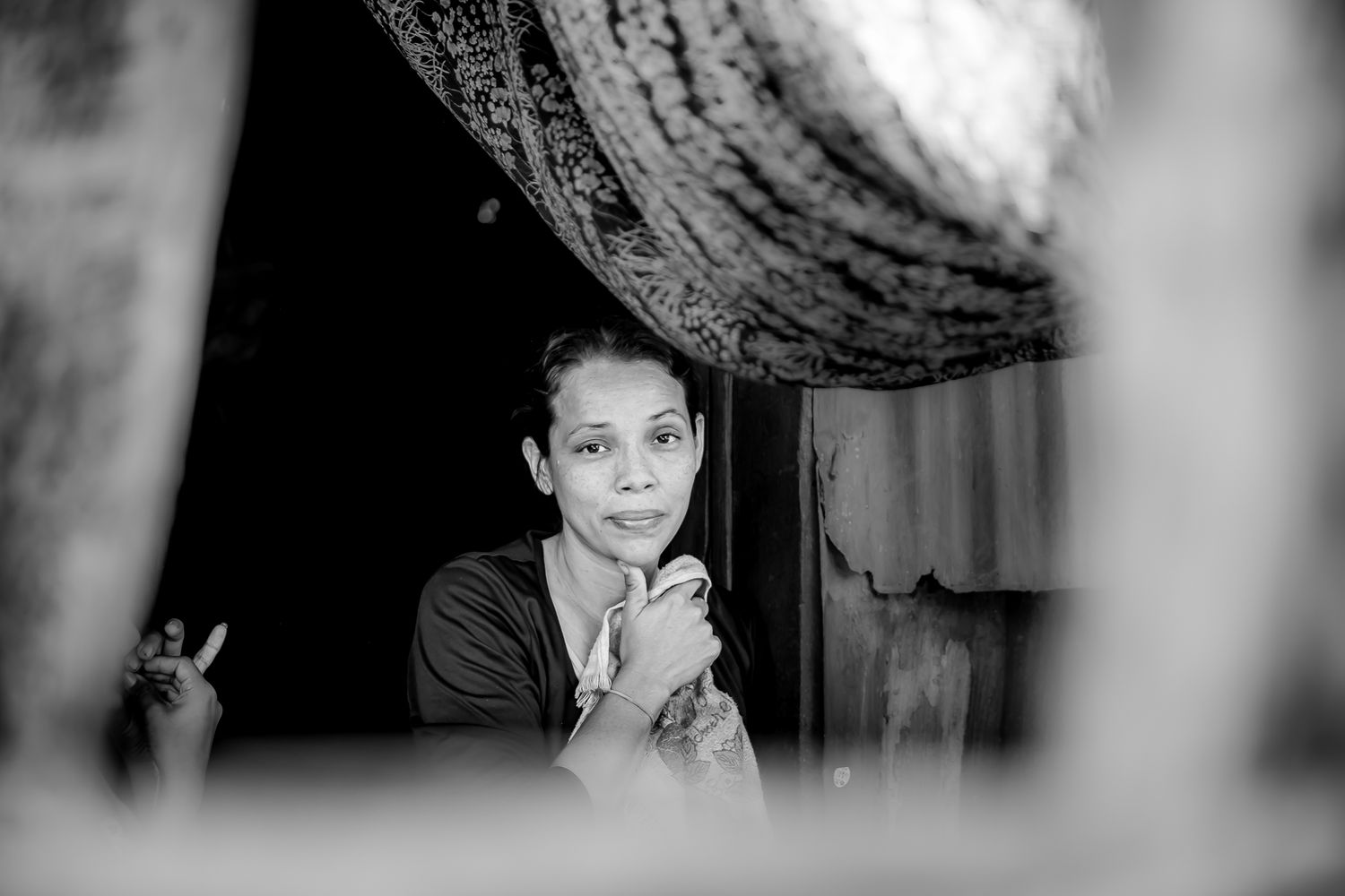 Black and white portrait of a woman framed by blurred foreground elements in a doorway.
