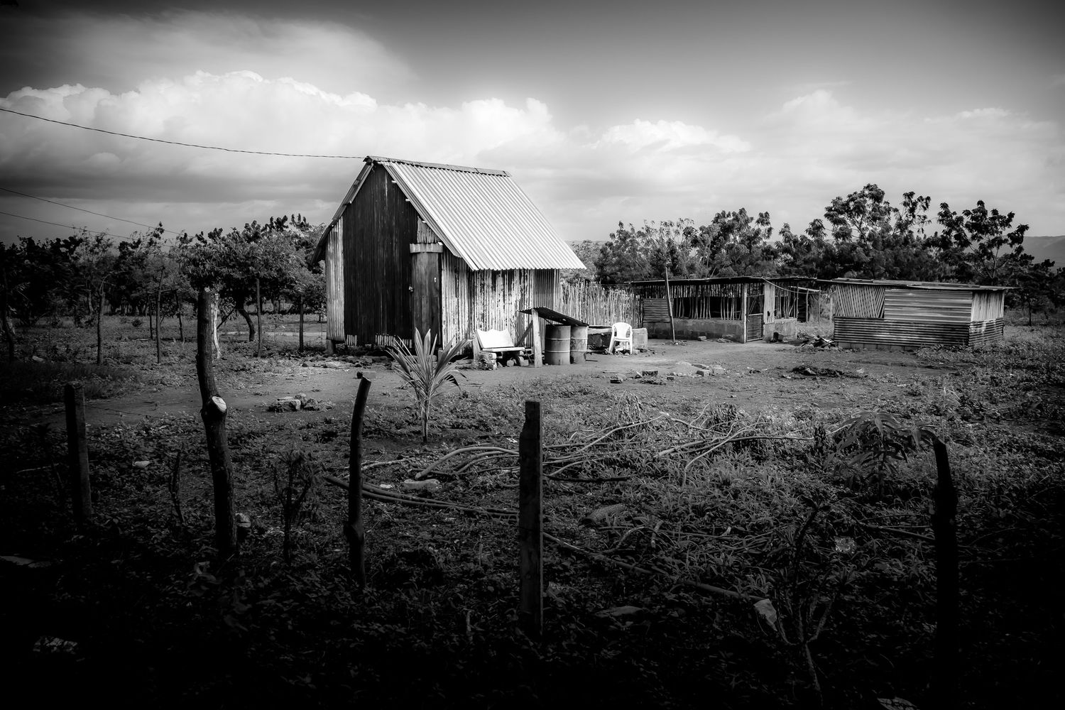 Black and white rural landscape featuring a weathered barn and farmhouse under a cloudy sky.