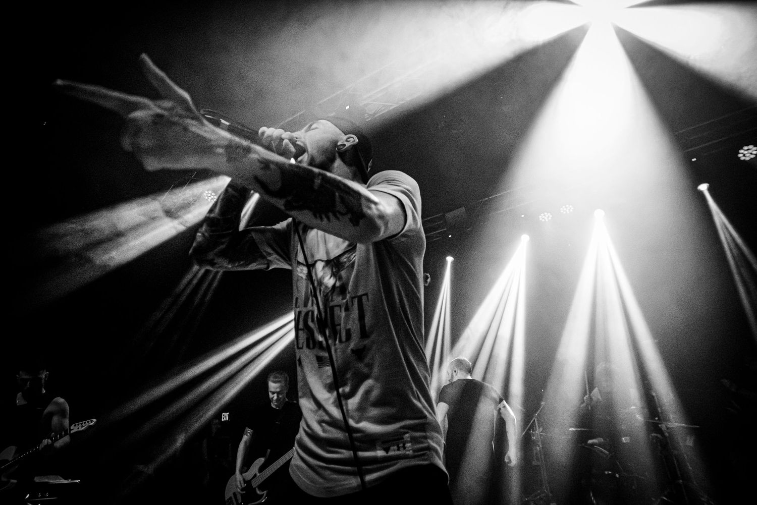 Black and white concert photo of a performer singing on stage surrounded by dramatic beam stage lighting.