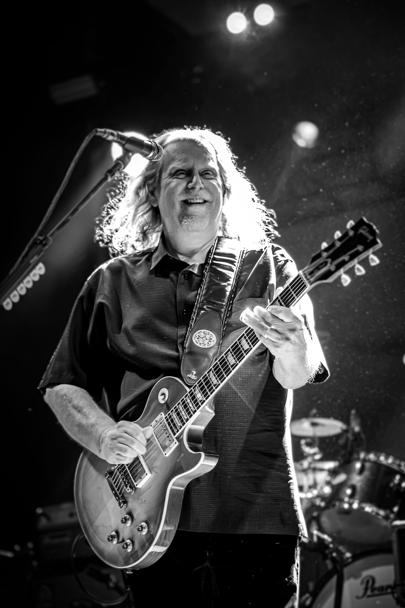 Black and white photo of a male guitarist performing on stage with a Gibson Les Paul electric guitar.