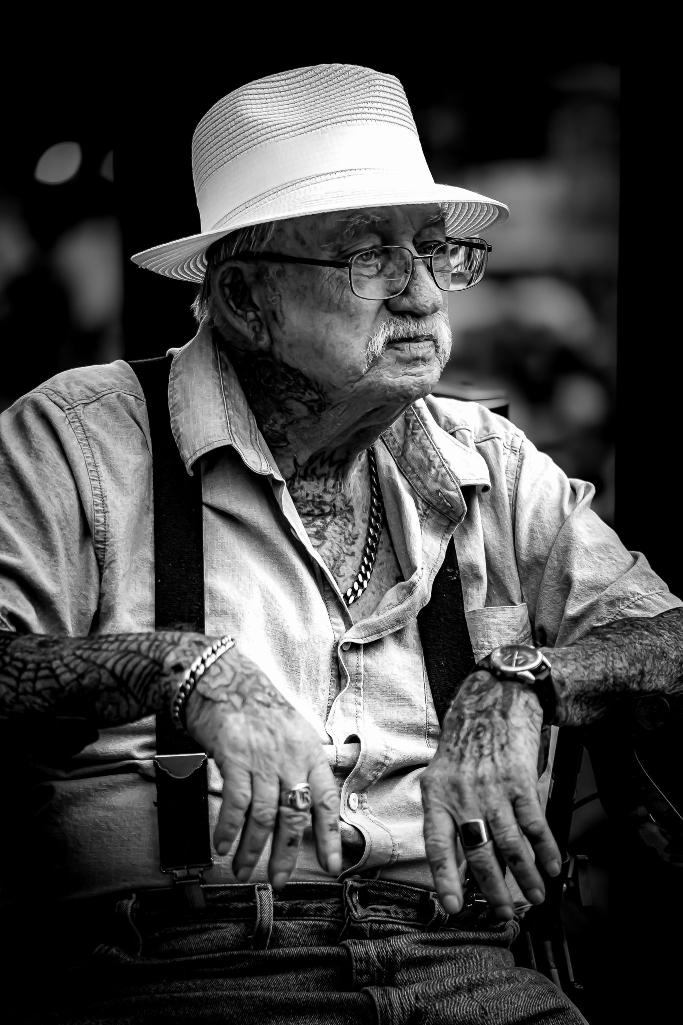 Black and white portrait of an elderly tattooed man wearing a white fedora, glasses, and suspenders.