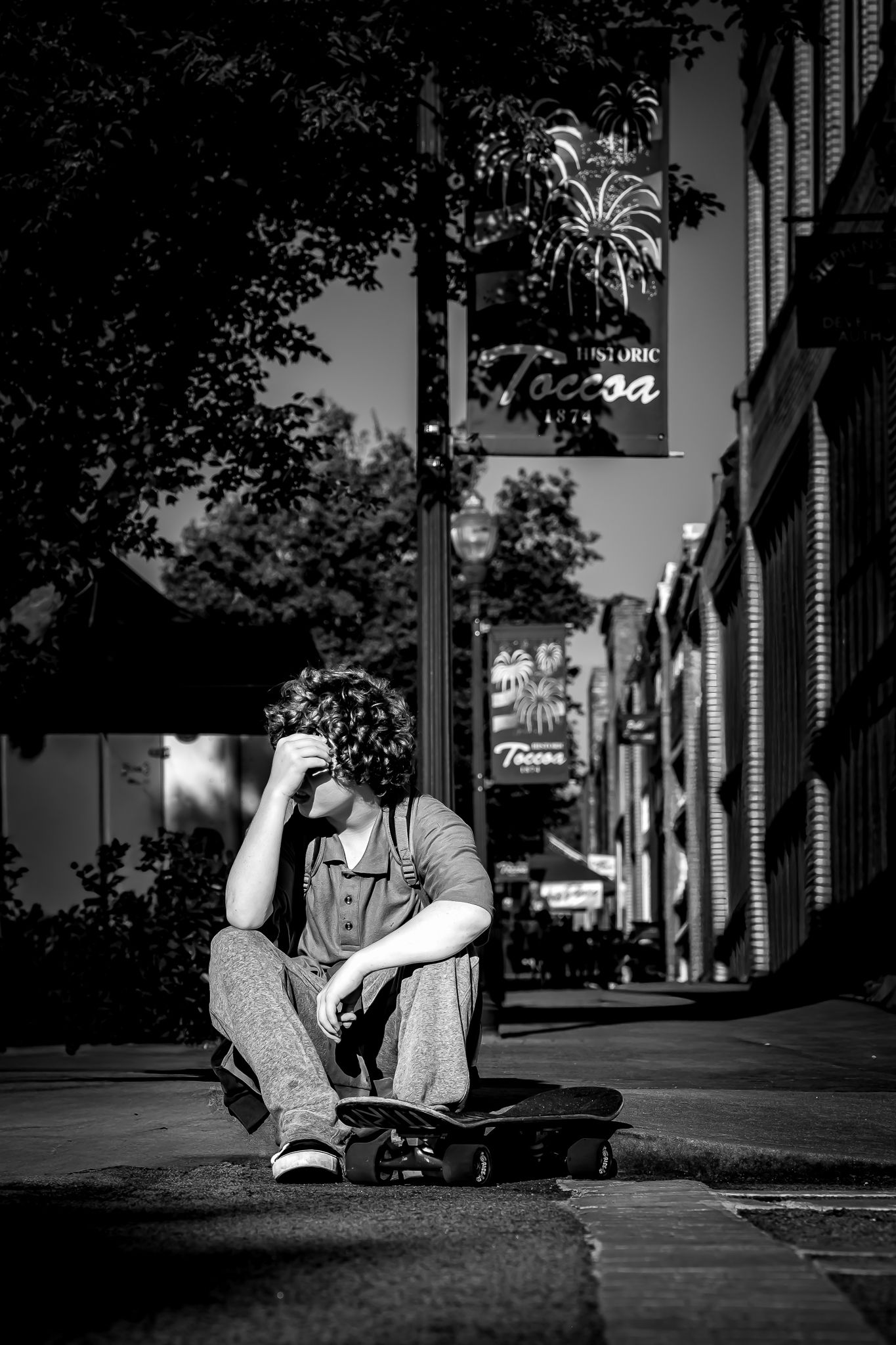Black and white photo of a young man sitting on a skateboard on a street in historic Toccoa, Georgia.