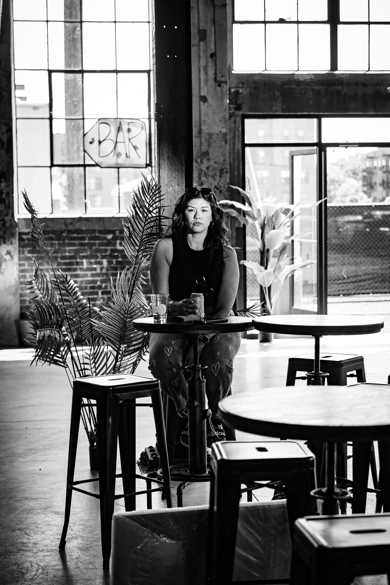 Woman sits alone at a table in an industrial bar in a black and white portrait photo.