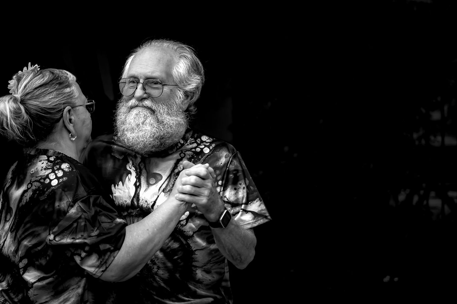 Elderly couple dancing together joyfully in black and white photo, man with white beard and glasses smiling warmly.