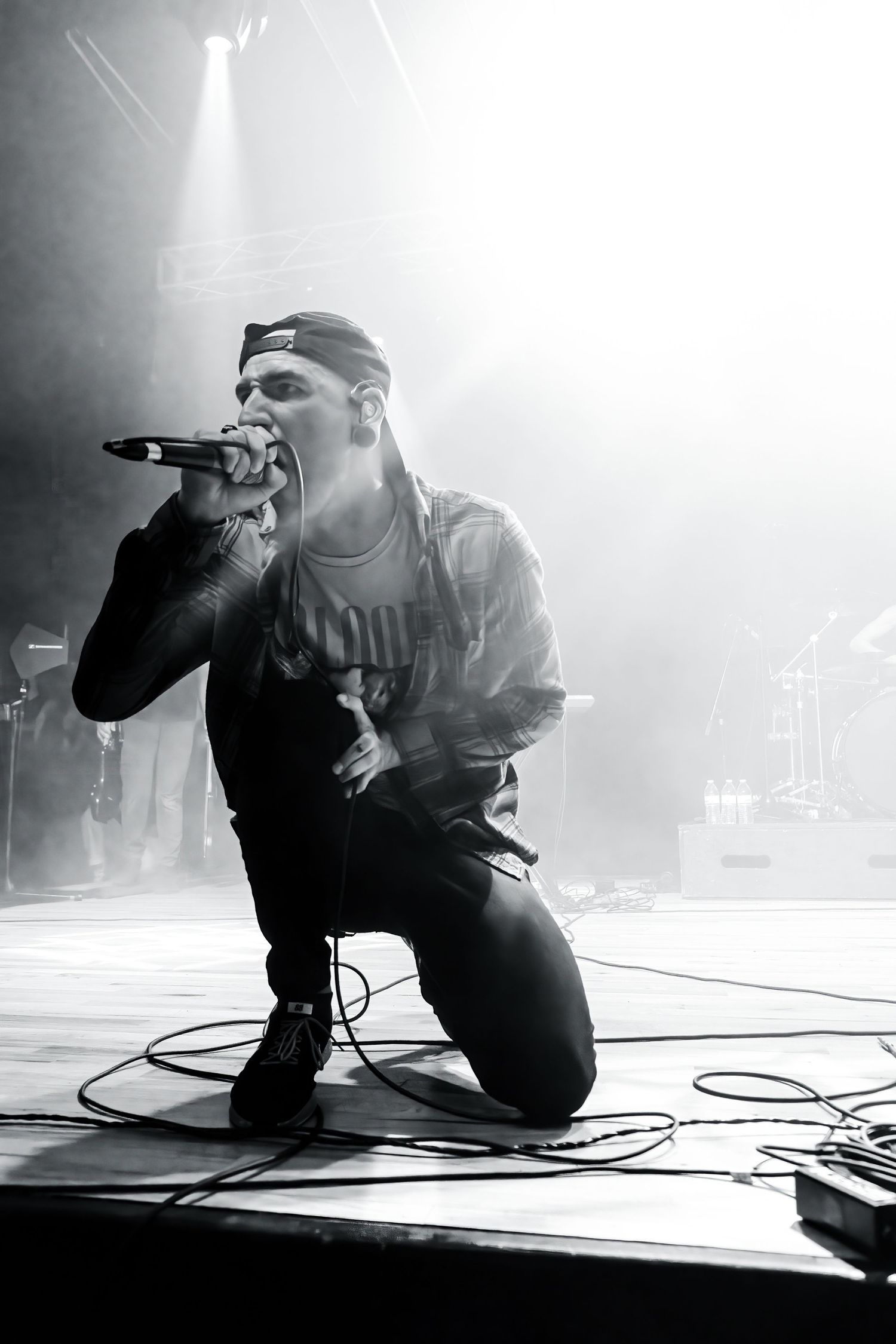 Black and white photo of a rapper kneeling on stage holding a microphone under dramatic stage lighting.