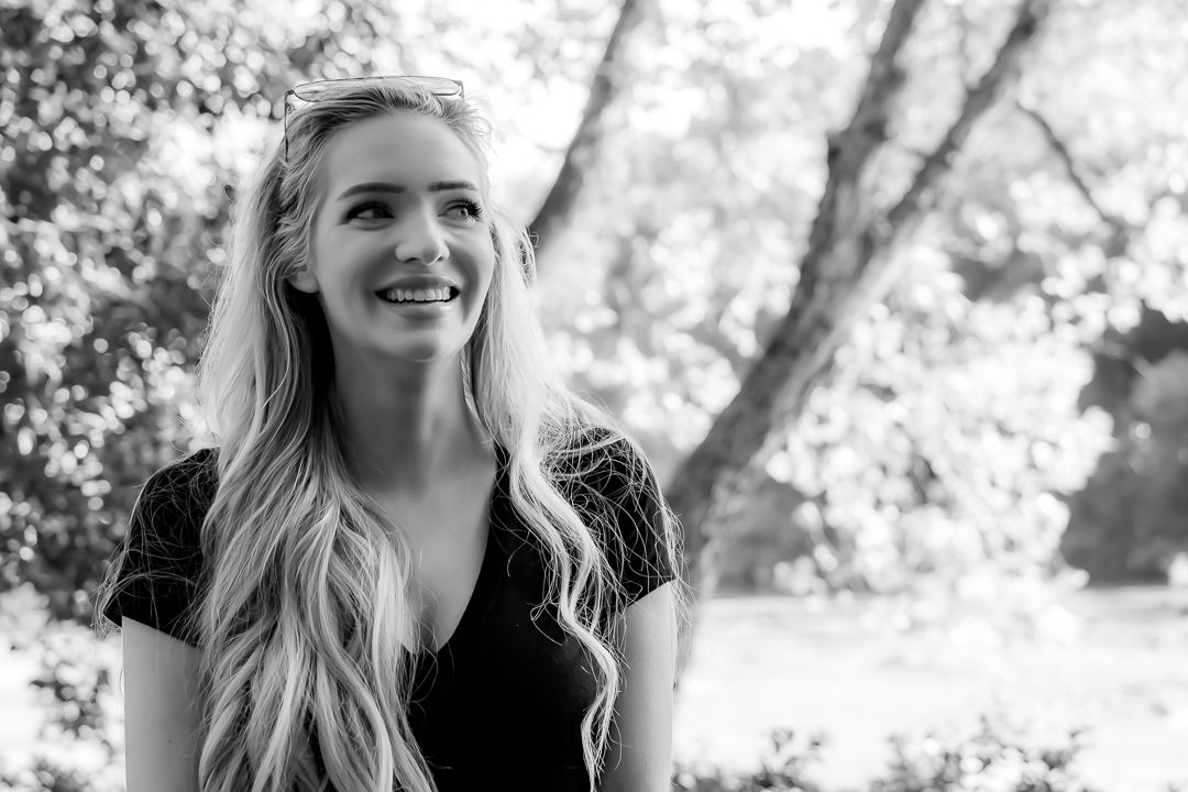 Smiling young blonde woman with long wavy hair outdoors in black and white.