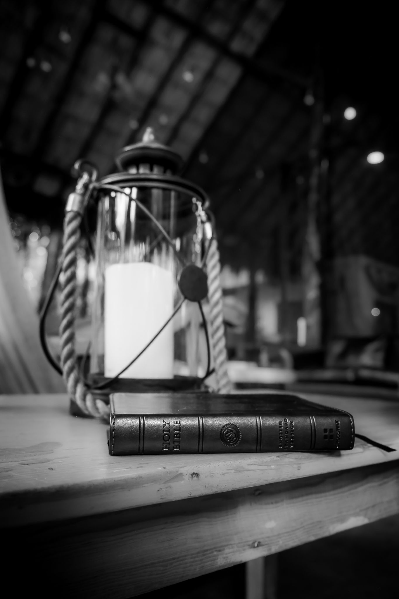 Black and white photo of a leather Bible beside a vintage rope lantern on a wooden table.