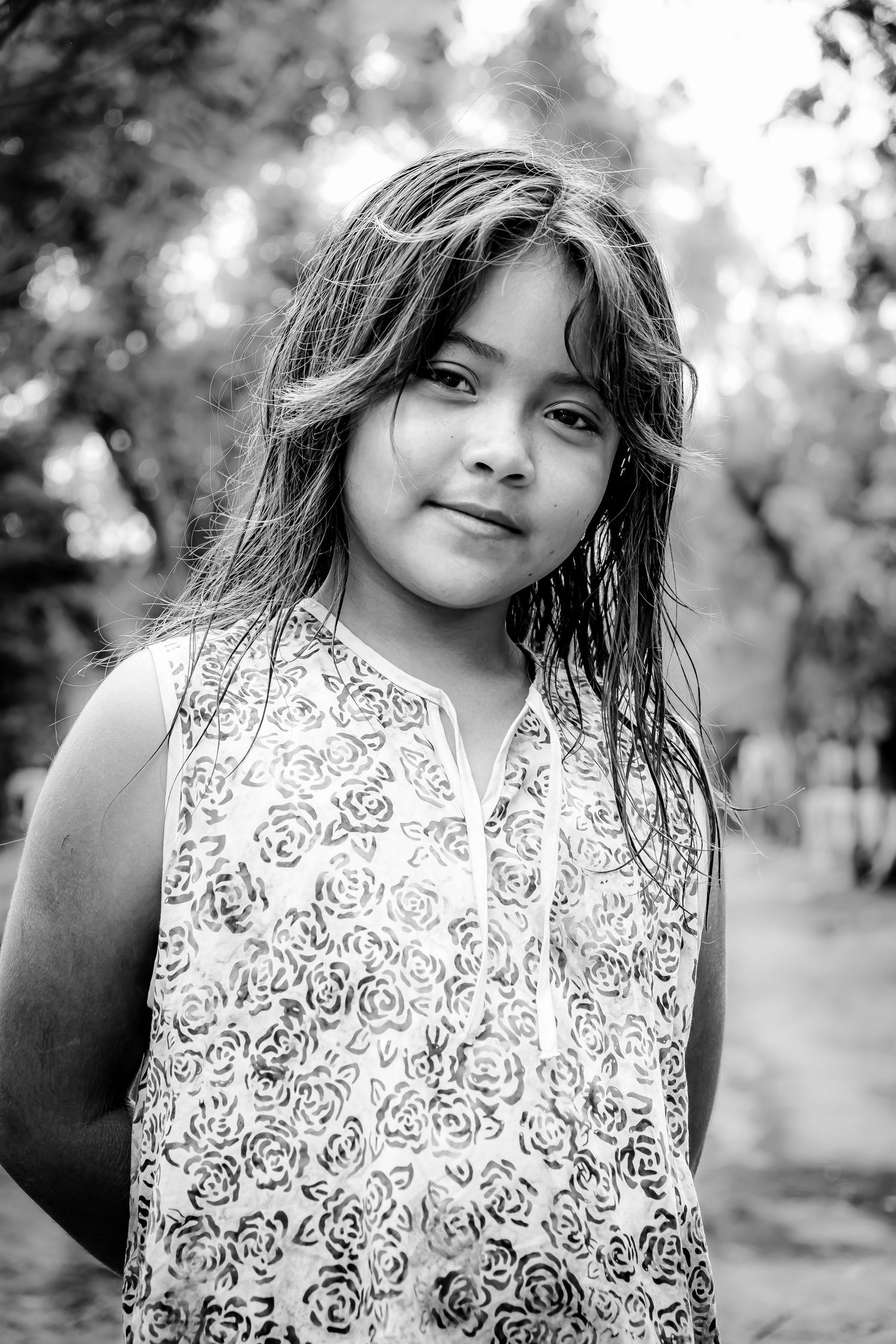 Black and white portrait of a young girl with long hair wearing a floral dress outdoors. Documentary photography. Missions coverage. Travel
