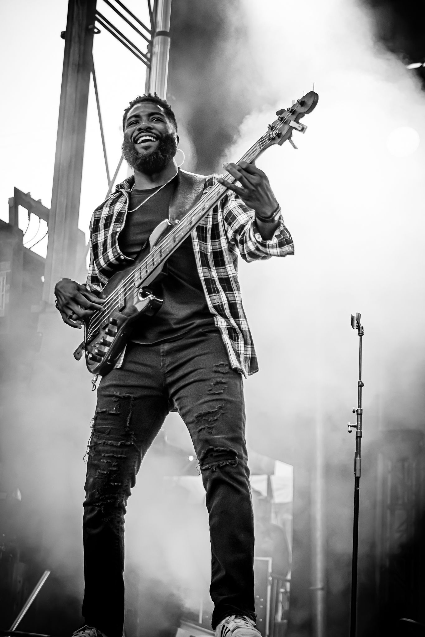 Smiling bassist plays electric guitar on a smoky stage in black and white concert photography.