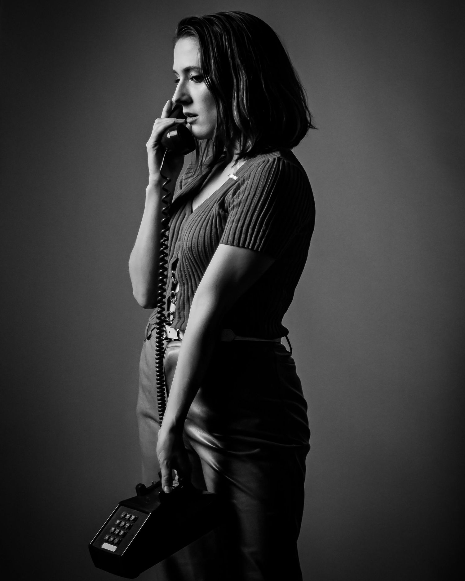 Woman in vintage style holds retro corded telephone in dramatic black and white studio portrait.